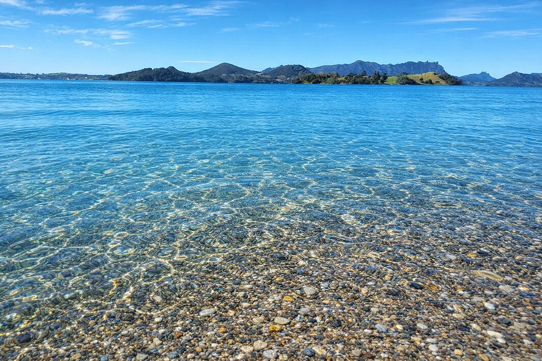 A clear lake with a rocky shore and distant mountains.