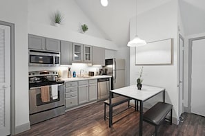 Een moderne keuken met grijze kastjes, roestvrijstalen apparatuur, een eettafel met stoelen en een hanglamp.