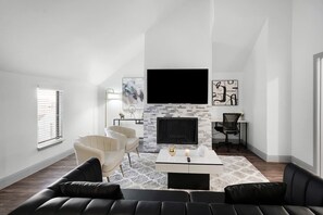 A modern living room with a fireplace, a flat-screen TV, and a dining area. - LUXE King Bed Getaway | Pool & Hot Tub | NRG & TMC (Houston)