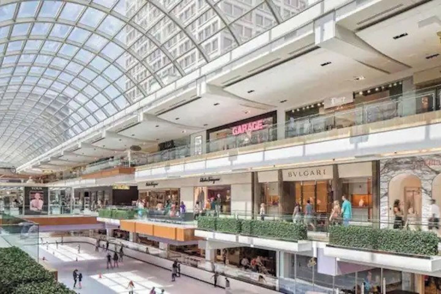 A multi-level shopping mall with a glass ceiling, featuring stores like BVLGARI and GARAGE.