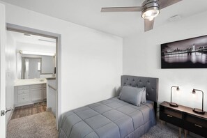 A bedroom with a bed, a nightstand, a desk, a chair, a ceiling fan, and a painting on the wall. - LUXE King Bed Getaway | Pool & Hot Tub | NRG & TMC (Houston)