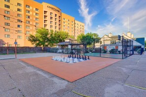 A courtyard with a chessboard set up, surrounded by a fence, with a hotel building in the background. - LUXE King Bed Getaway | Pool & Hot Tub | NRG & TMC (Houston)