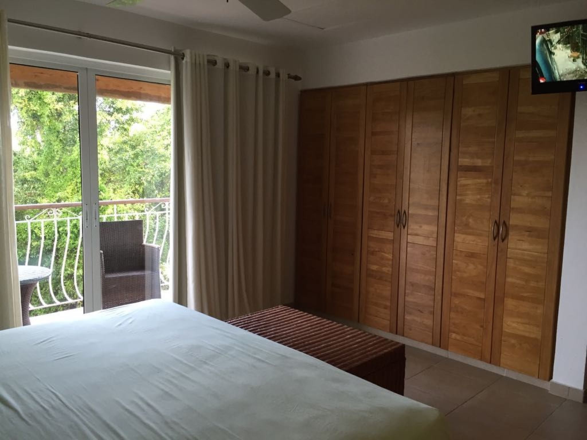 Ein Schlafzimmer mit einem Bett, einem Holzschrank, einem Balkon mit Tisch und Stühlen sowie einem an der Wand befestigten Fernseher.