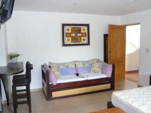 A room with a sofa, a small table, a chair, a bed, and a door.