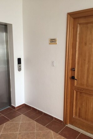 A hallway with a wooden door, a wall-mounted elevator control panel, and a floor with patterned tiles.
