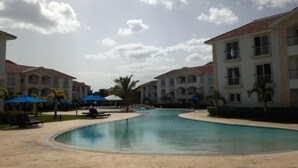 A resort pool area with a clear sky, palm trees, and a building with multiple balconies. - Unknown Accommodation by Interhome (Bayahibe)