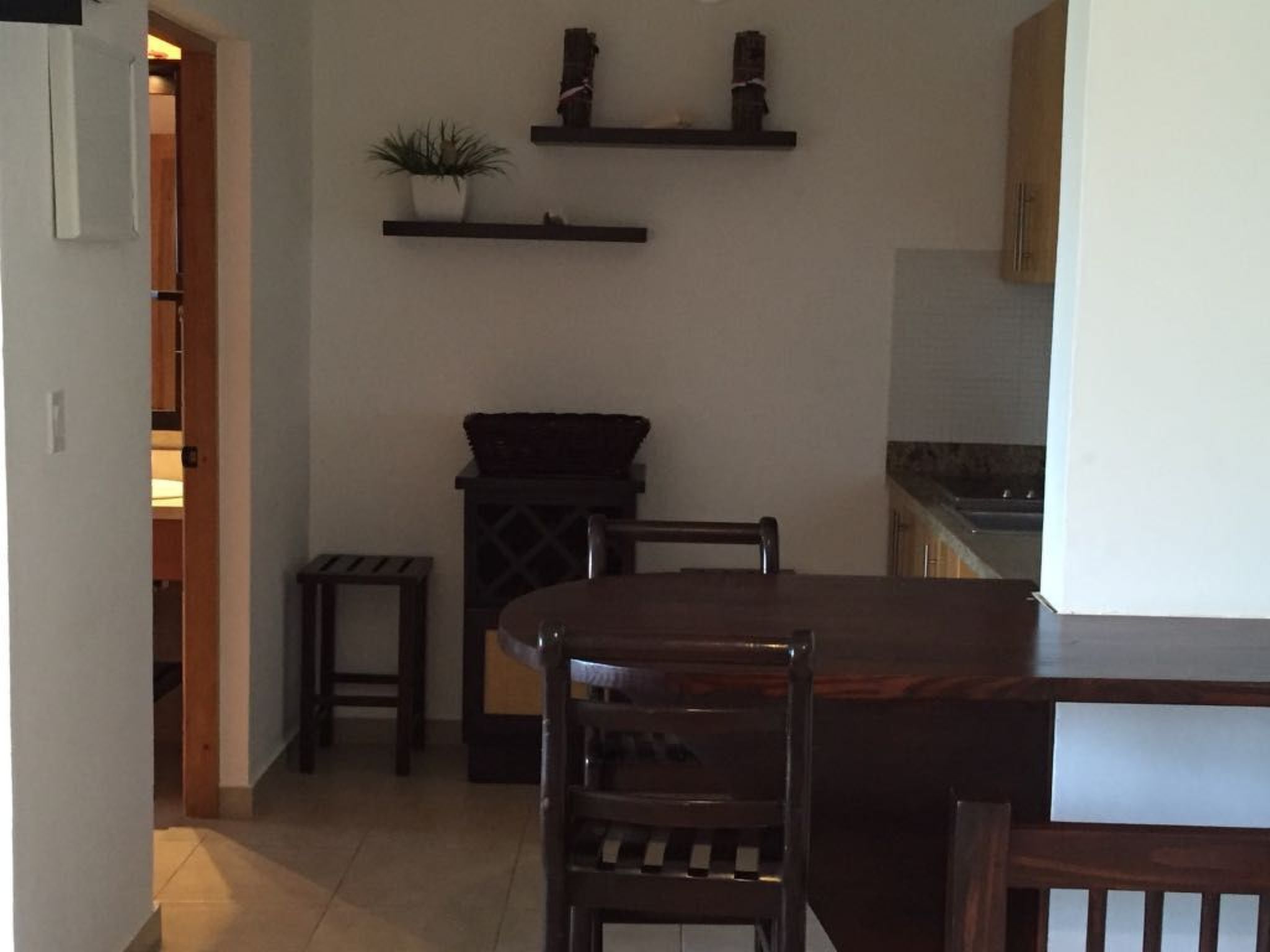 Una cocina con una mesa y sillas de madera, un armario pequeño y dos estanterías con plantas en macetas.