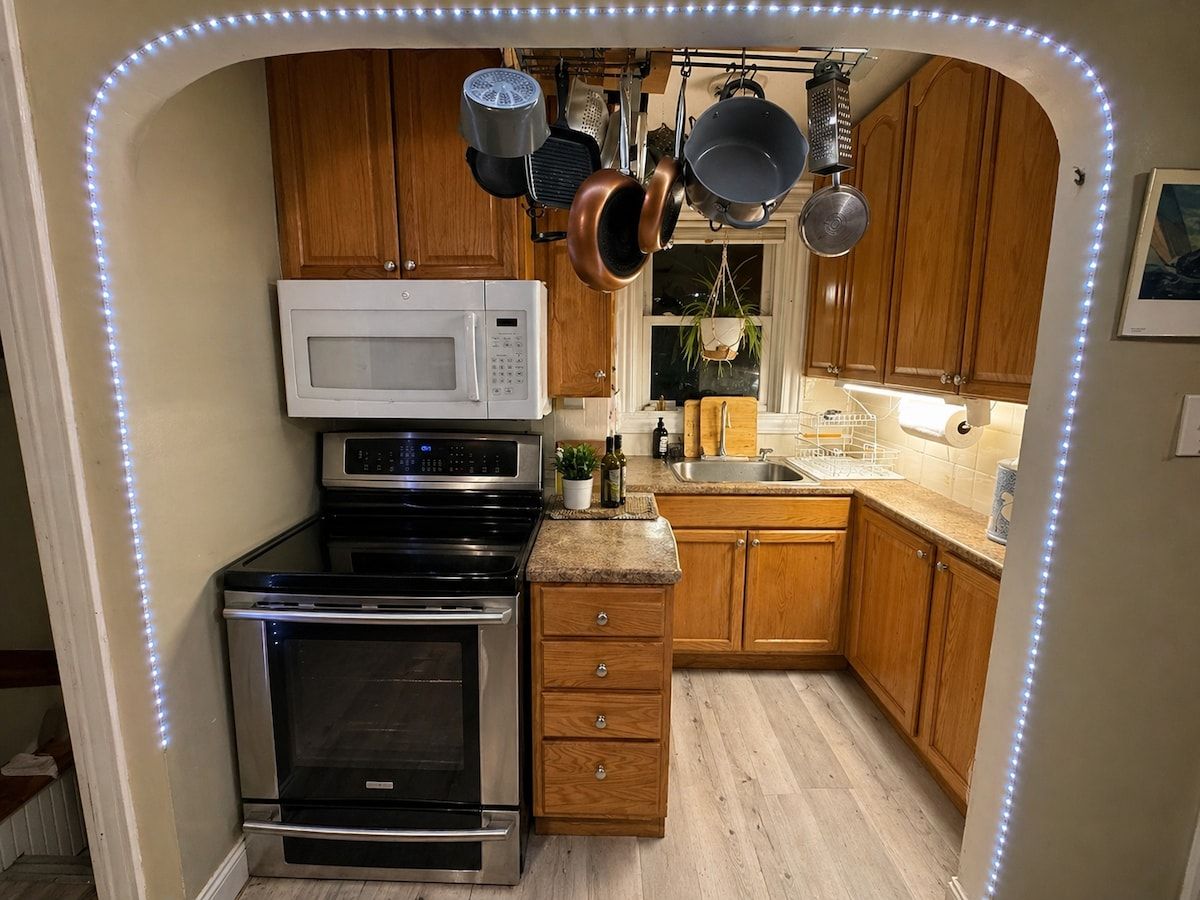 A compact kitchen with a microwave, oven, and hanging pots.