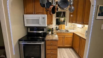 A compact kitchen with a microwave, oven, and hanging pots.