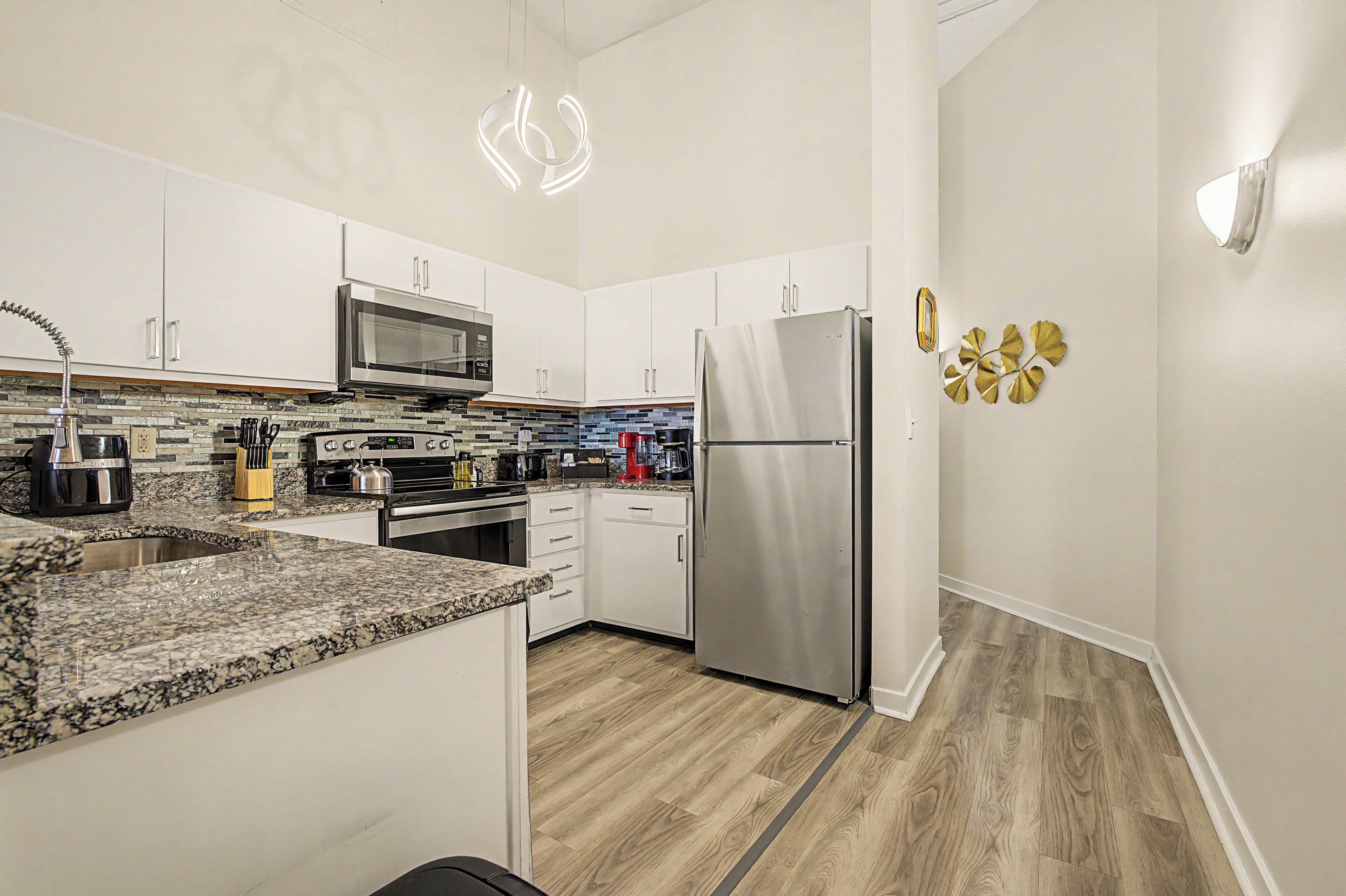 A modern kitchen with white cabinets, a stainless steel refrigerator, a microwave, and a granite countertop.