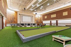 Une salle de billard dotée d’un revêtement de sol vert en gazon synthétique, d’une table de billard et de coins salon.