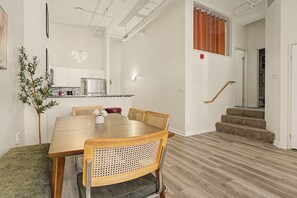 Un comedor con una mesa y sillas de madera, una cocina al fondo y una escalera que sube a un nivel superior.