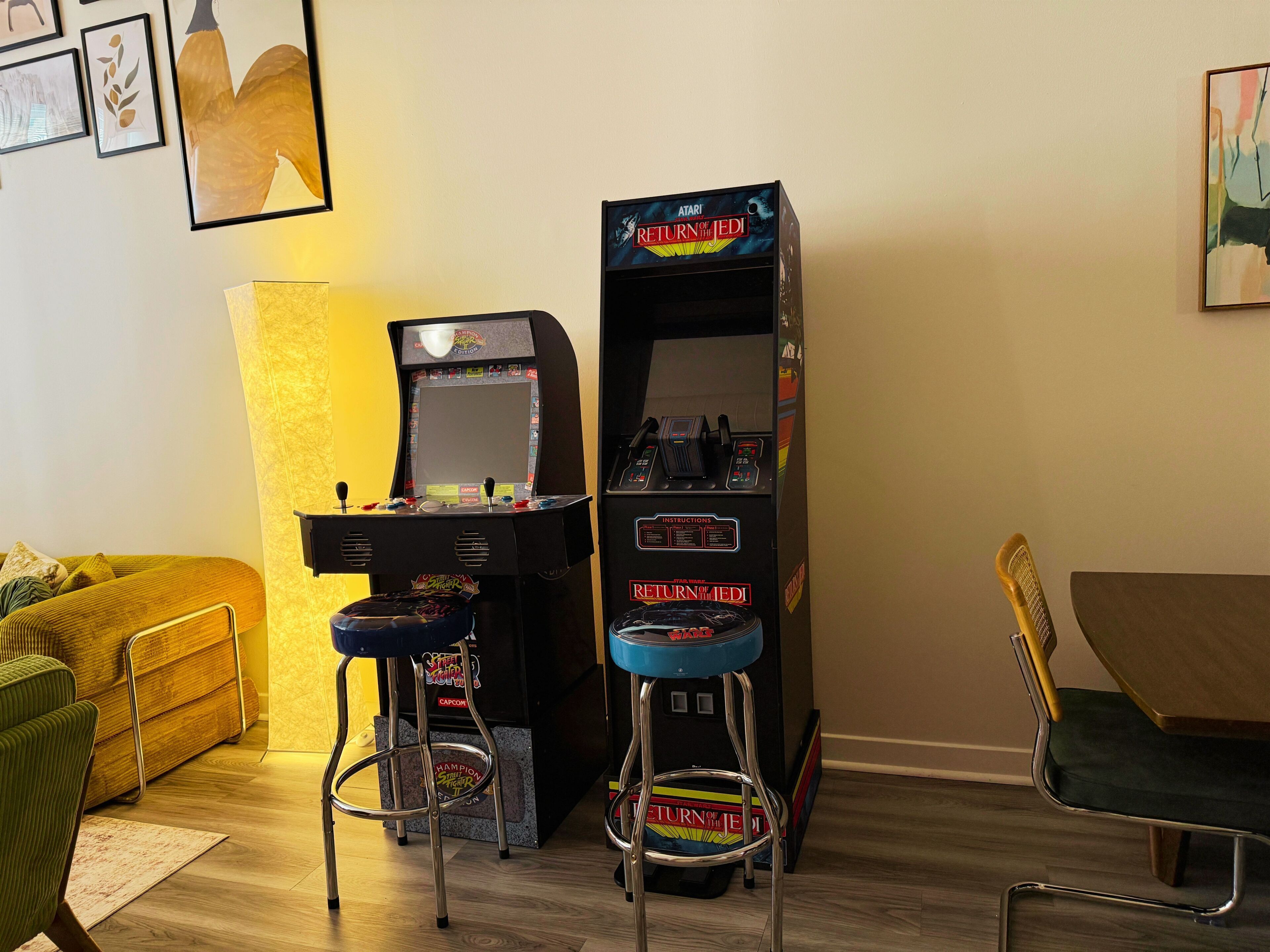 Een kamer met een gameconsole, twee krukken, een bank en een tafel.