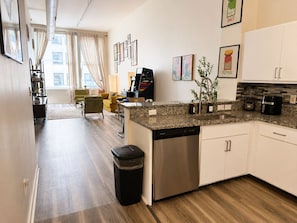 Eine moderne Küche mit Geschirrspüler, Kaffeemaschine und Spüle. Es gibt einen Essbereich mit einem gelben Stuhl und einer Couch.