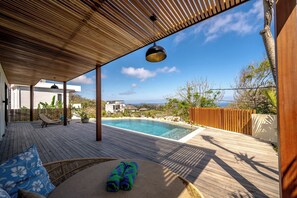 A wooden deck with a pool, lounge chairs, and a view of the ocean. - Villa LIMA 2 Uluwatu (Pecatu)