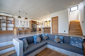 A modern living space with a sectional sofa, a dining area, kitchen, and a staircase. - Villa LIMA 2 Uluwatu (Pecatu)
