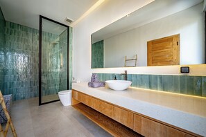 Een moderne badkamer met een douchecabine van glas, een witte wastafel en een houten opbergmeubel.