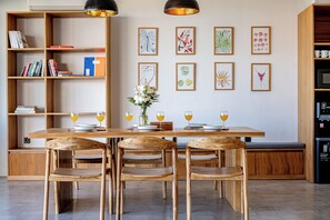A modern kitchen with wooden furniture, a dining table set for four, and a bookshelf filled with books and decorative items. - Villa LIMA 2 Uluwatu (Pecatu)