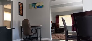 A living room with a brown leather chair, a black office chair, a red and white patterned rug, and a painting on the wall. - Your Windsor Home Away from Home | 3BR One-Storey (Windsor)