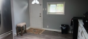 A room with a door, a window, a small stool, and a trash bin. - Your Windsor Home Away from Home | 3BR One-Storey (Windsor)