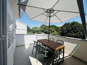 Een balkon met een tafel, stoelen en een parasol, met uitzicht op bomen.