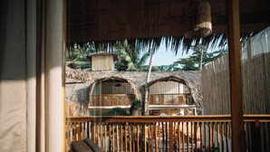 A wooden balcony with a thatched roof, overlooking a garden with a water feature and a wooden structure. - Laya El Nido (El Nido)