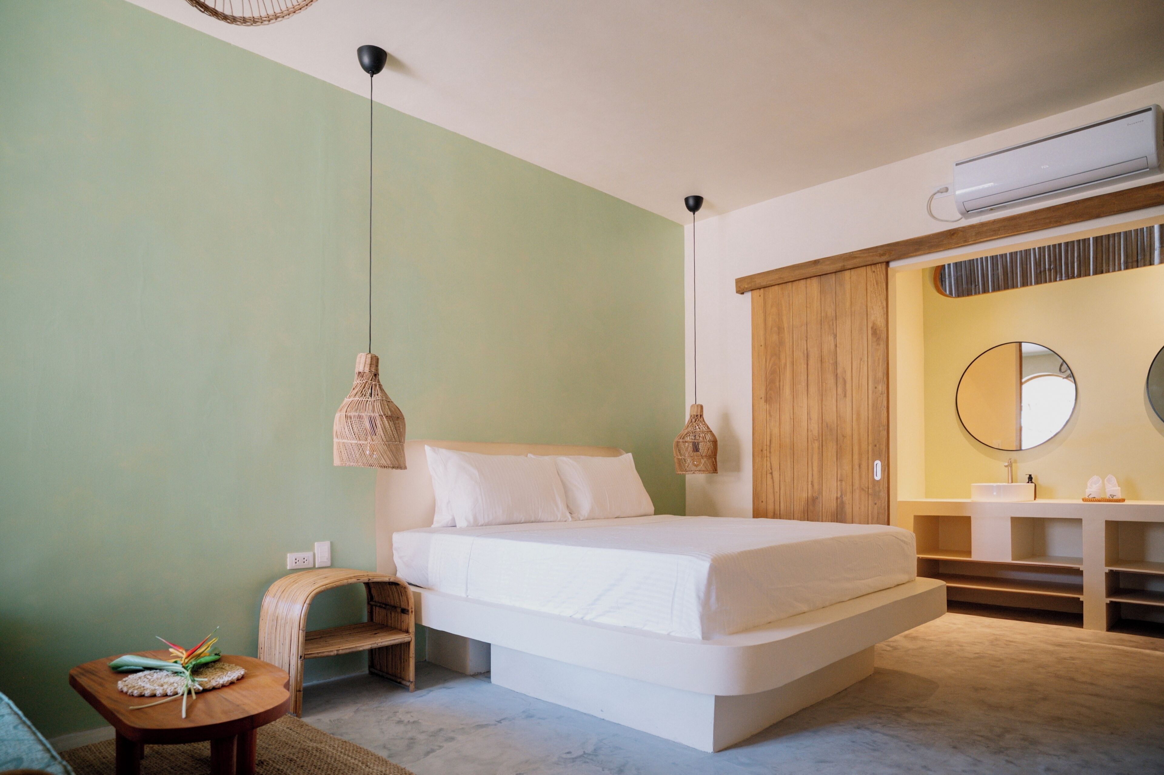 Quarto com cama, mesa de cabeceira e uma pequena mesa redonda com um objeto decorativo.