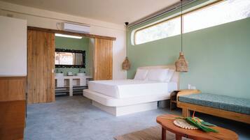 A bedroom with a bed, a wooden bench, a small table, a window with a view, and a bathroom with a mirror and sink.