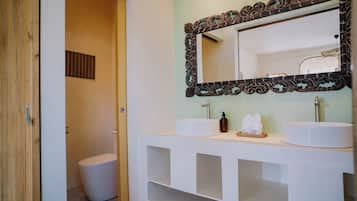 A bathroom with a wooden door, a white toilet, and a vanity with two sinks and a mirror.