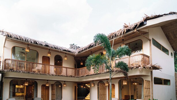 A multi-level building with a thatched roof, wooden balconies, and a central courtyard with seating and plants. - Laya El Nido (El Nido)