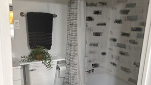 Ein Badezimmer mit Toilette, einer Duschvorhang mit Muster, einem Handtuchhalter mit schwarzem Handtuch und einer kleinen Pflanze auf dem Waschbecken.