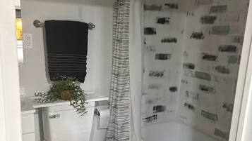 Un baño con inodoro, cortina de ducha estampada, toallero con toalla negra y una planta pequeña sobre el lavamanos.