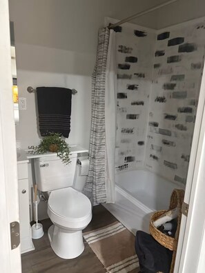 A bathroom with a toilet, a shower curtain with a pattern, a towel rack with a black towel, and a small plant on the sink. - Peaceful Private Pet Friendly Studio-10 Miles from Buc-ee's & I65 (Harvest)