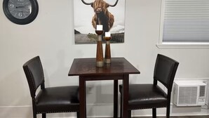 Ein Essbereich mit Tisch und zwei Stühlen, einer Uhr, einer Kunstszene zum Thema Stier und einem Fenster mit Jalousien.