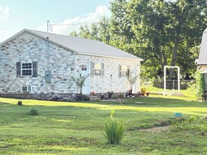 A single-story house with a sloped roof, a brick exterior, and a front porch with potted plants.
