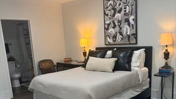 Ein Schlafzimmer mit einem Bett, zwei Nachttischlampen, einem Deckenventilator und einem großen abstrakten Gemälde an der Wand.