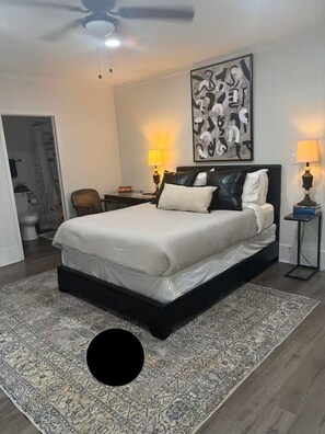 Een slaapkamer met een bed, twee bedlampen, een plafondventilator en een groot abstract schilderij aan de muur.