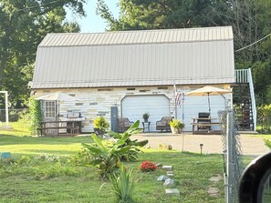 A rustic barn-style building with a large garage door, outdoor seating area, and a flagpole.