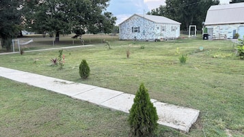 A grassy area with a stone building, a fenced sports field, and a small tree.