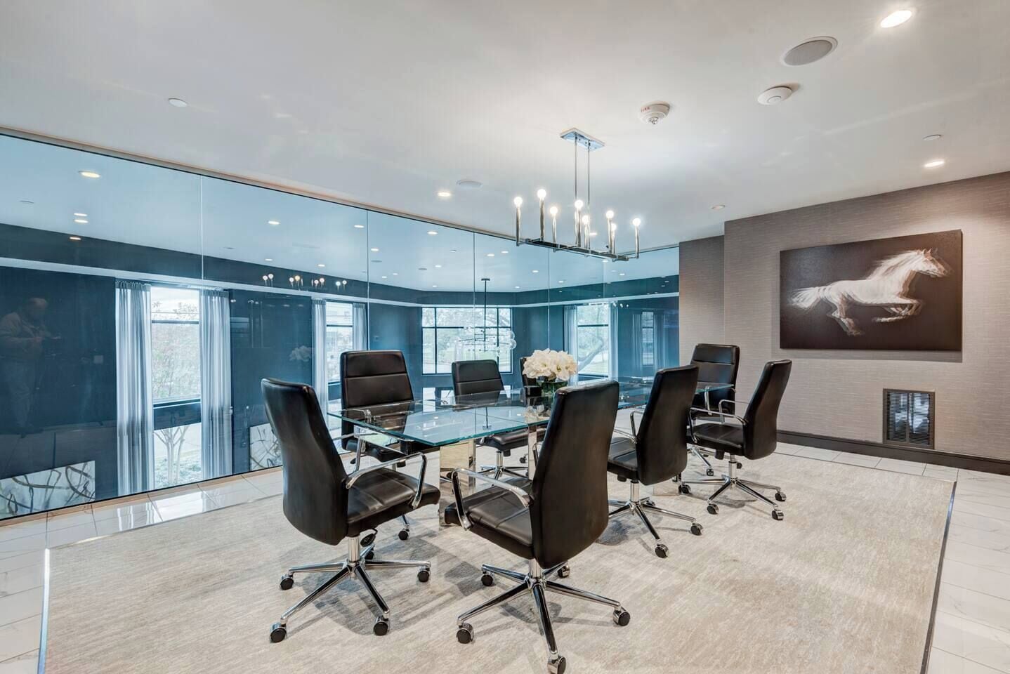 A modern conference room with a glass table, black chairs, and a mounted artwork of a horse.