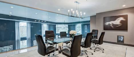 Une salle de conférence moderne avec une table en verre, des chaises noires et une œuvre d’art représentant un cheval, accrochée au mur.