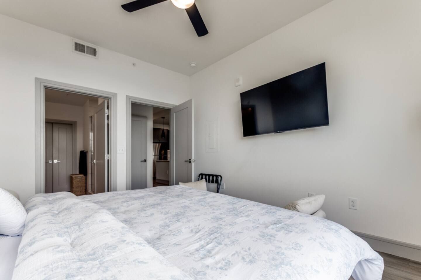 A bedroom with a large bed, a ceiling fan, a TV mounted on the wall, and a wardrobe.