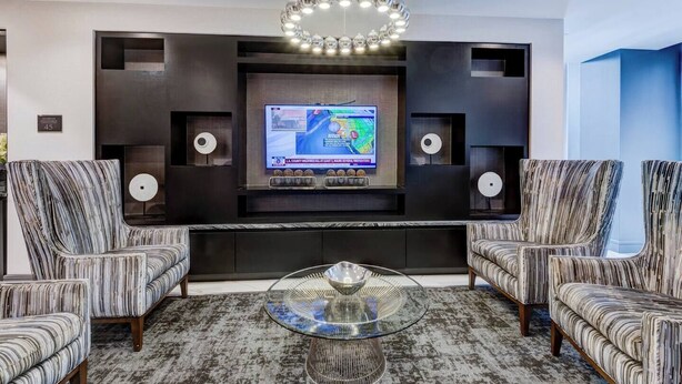 Een moderne woonkamer met een groot flatscreen-televisie bevestigd aan een donkere muur, omringd door twee fauteuils en een salontafel.