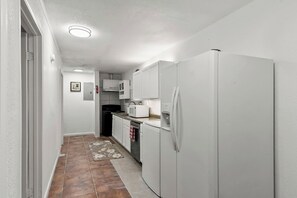 A narrow kitchen with white cabinets, a refrigerator, a microwave, and a sink. - Furnished 3BR/2BA Near UA — Monthly Stays (Tuscaloosa)