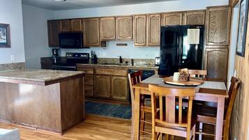A kitchen with wooden cabinets, a black refrigerator, a microwave, and a dining area with a wooden table and chairs.