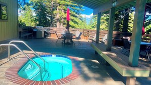 Et overdækket udendørs swimmingpool med træterrasse, grillområde og spisebord med stole.