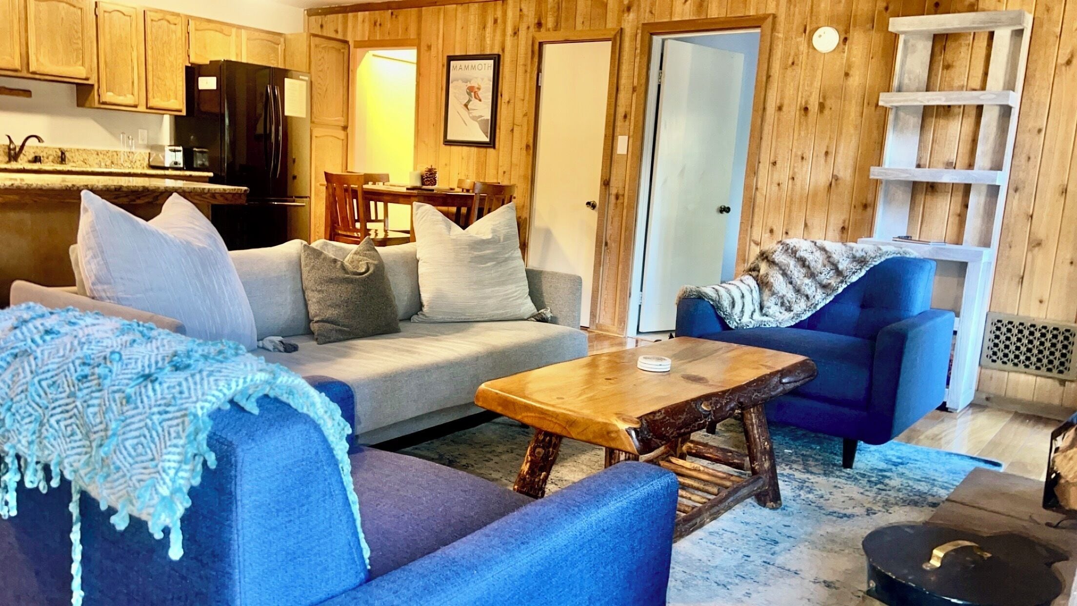 A cozy living room with a sofa, a blue armchair, a wooden coffee table, and a fireplace.