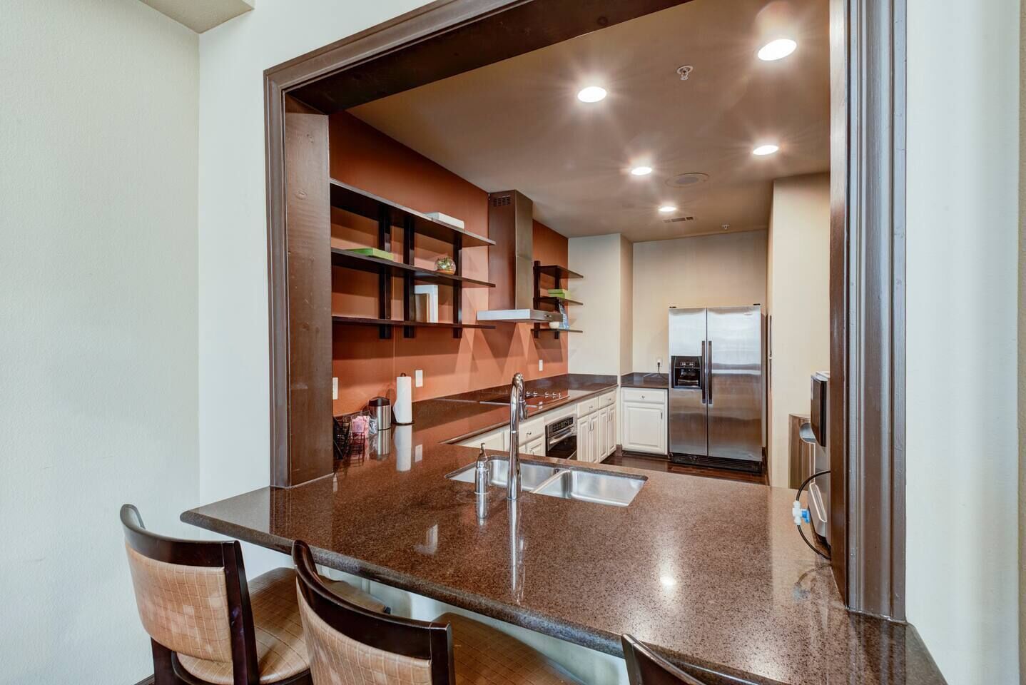 A modern kitchen with a central island, built-in shelves, and a stainless steel refrigerator.