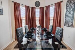 A dining area with a glass table, black chairs, and a clock on the wall. - 2BD Pumpkin King Retreat |NRG & TMC| Pool & Patio (Houston)