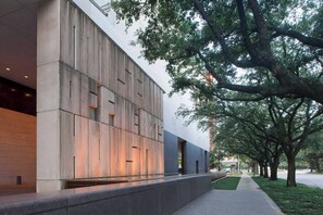 A modern building with a flat facade, large windows, and a tree-lined pathway. - 2BD Pumpkin King Retreat |NRG & TMC| Pool & Patio (Houston)